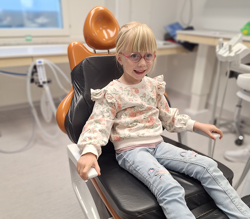 Flicka sitter i tandläkarstol och ser glad ut.