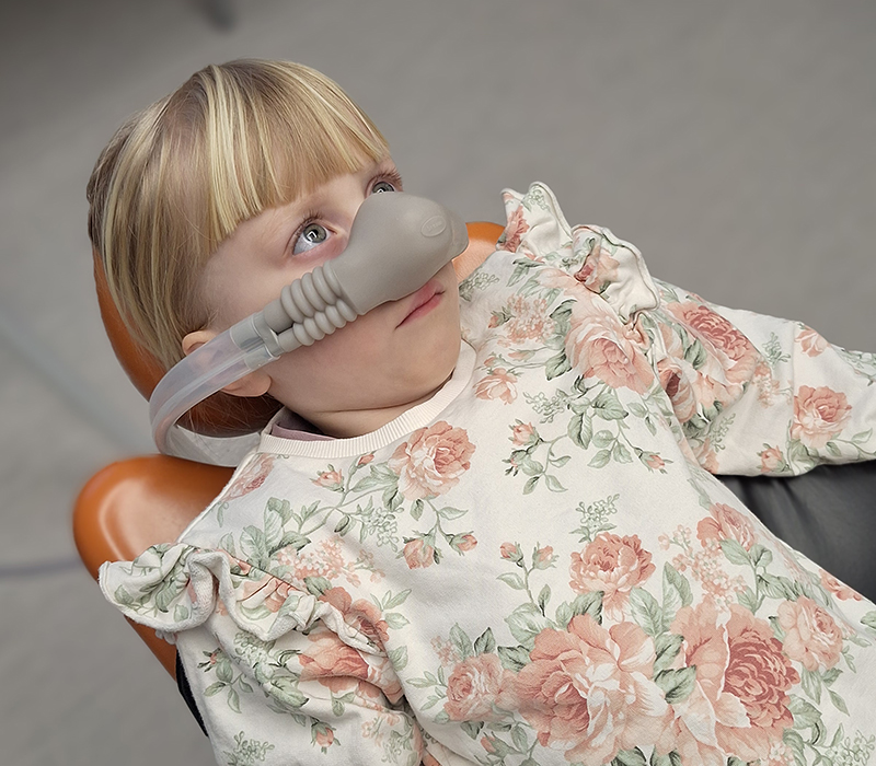 Flicka ligger ner i tandläkarstol med en mask över näsan.