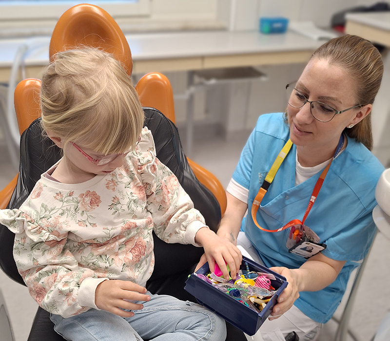 En flicka sitter i tandläkarstolen och får välja leksak ur en låda med saker.
