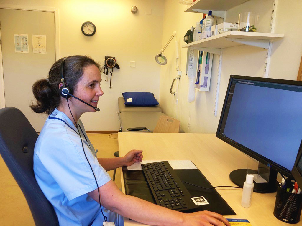 Sjuksköterska med hörlurar sitter framför en dataskärm