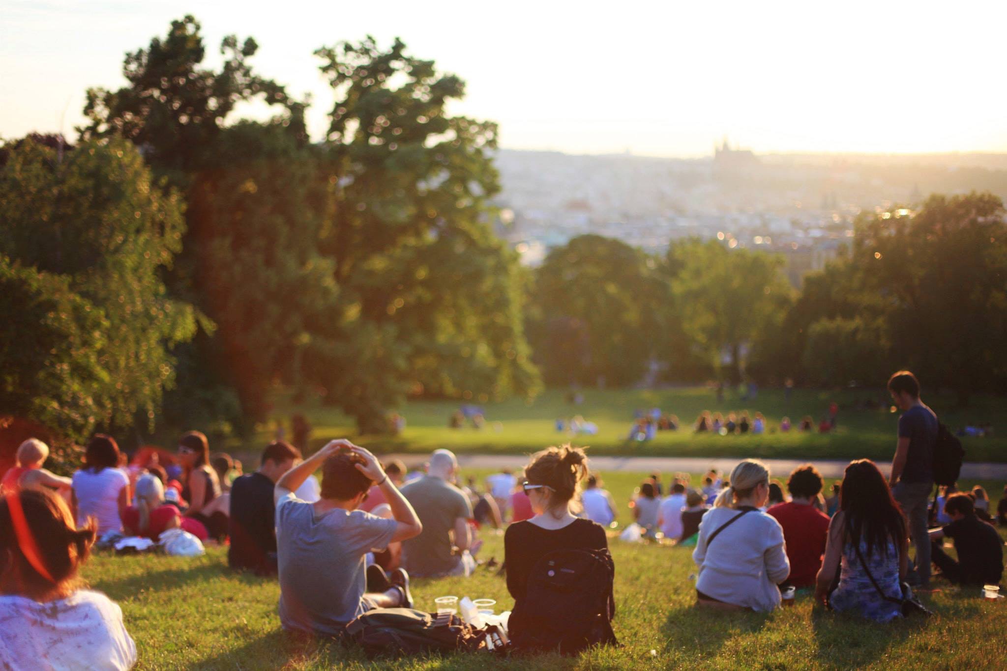 Ett stort antal människor sitter på gräsmattan i en park under en sommarkväll.