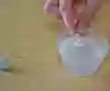 En hand som lägger ner en gjuten insats från en hörapparat i ett glas med vatten och diskmedel. 