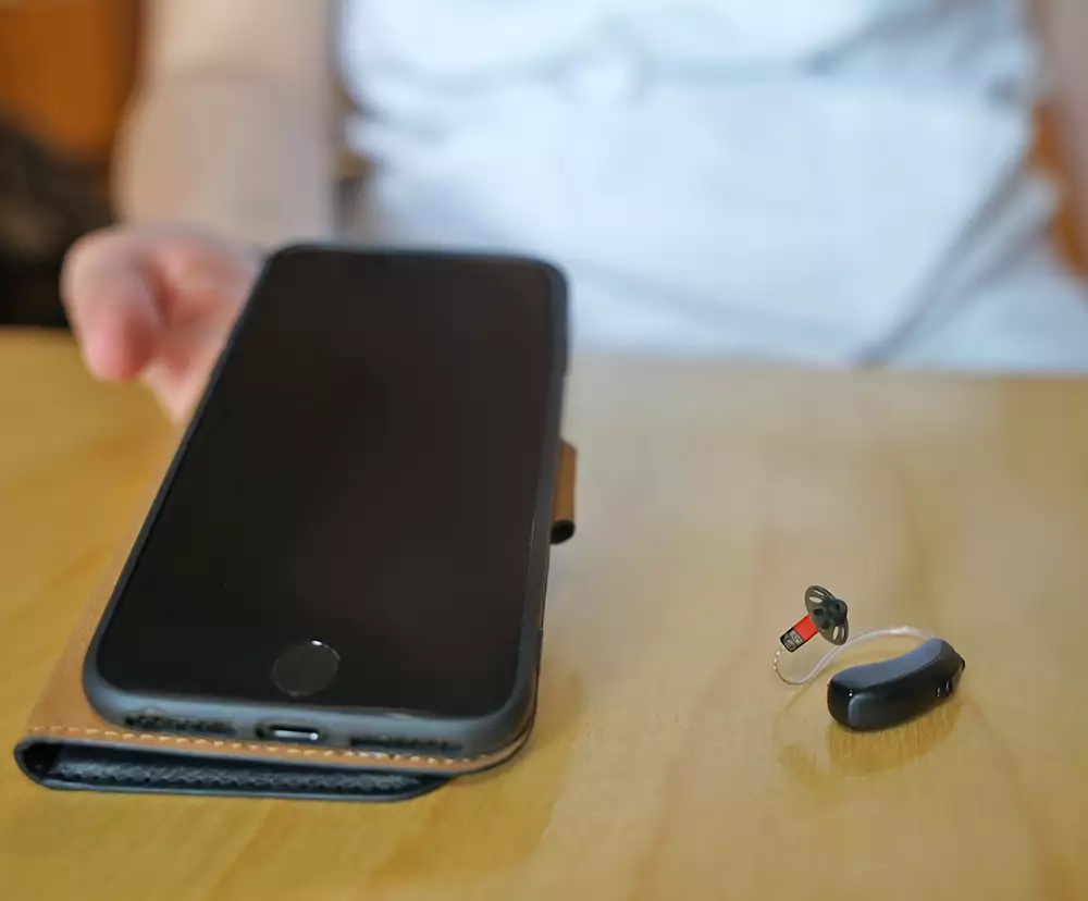 En telefon och en hörapparat ligger på ett bord.