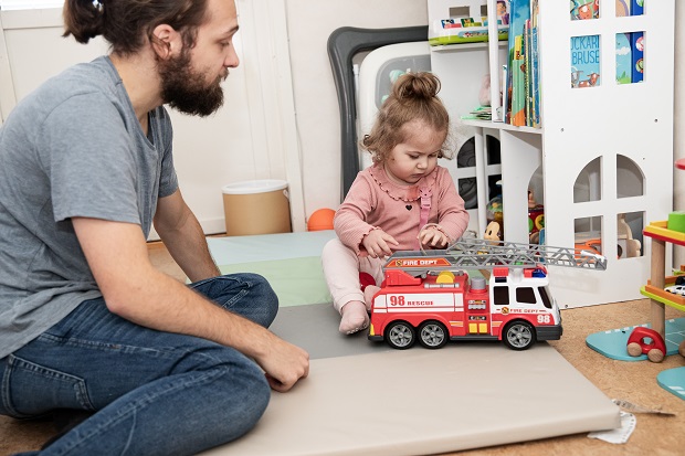 Pappa och ett litet barn sitter på golvet och leker med en brandbil.