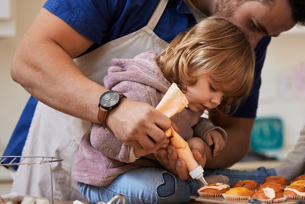En förälder som hjälper ett barn att spritsa kristyr på muffins.