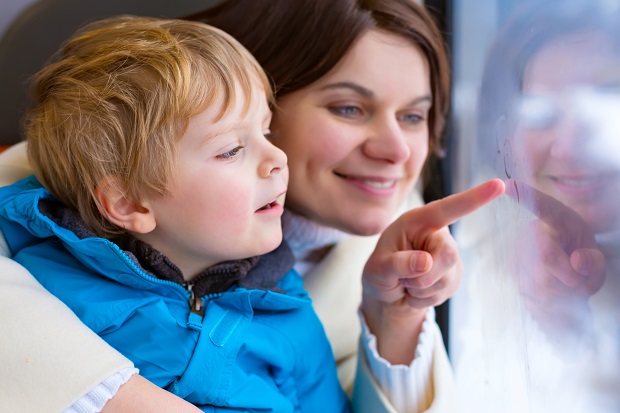 Ett litet barn och en mamma tittar ut från ett fönster och pekar.