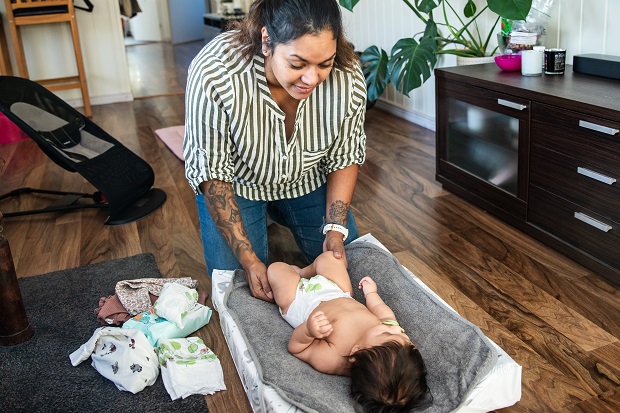 Mamma byter blöja på sitt barn på golvet i vardagsrummet.