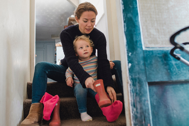 Mamma sitter i en trapp med ett barn och hjälper till att ta på stövlar.