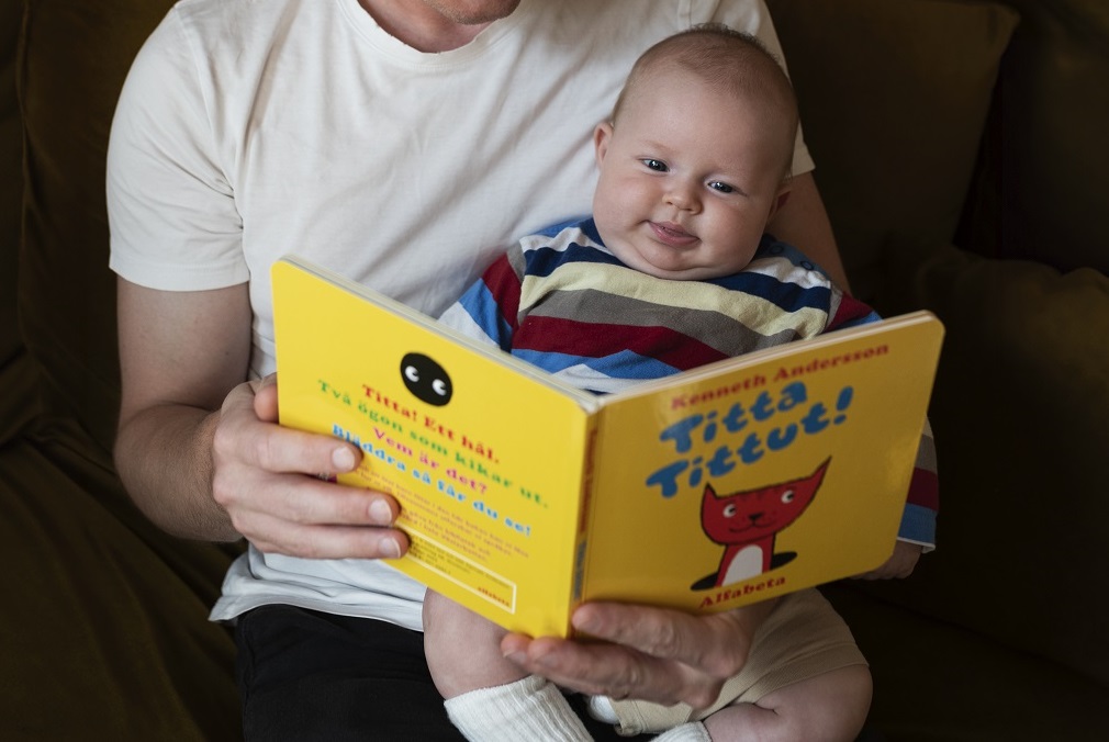 Bebis som sitter i knä på en vuxen och tittar i boken Titta titut.