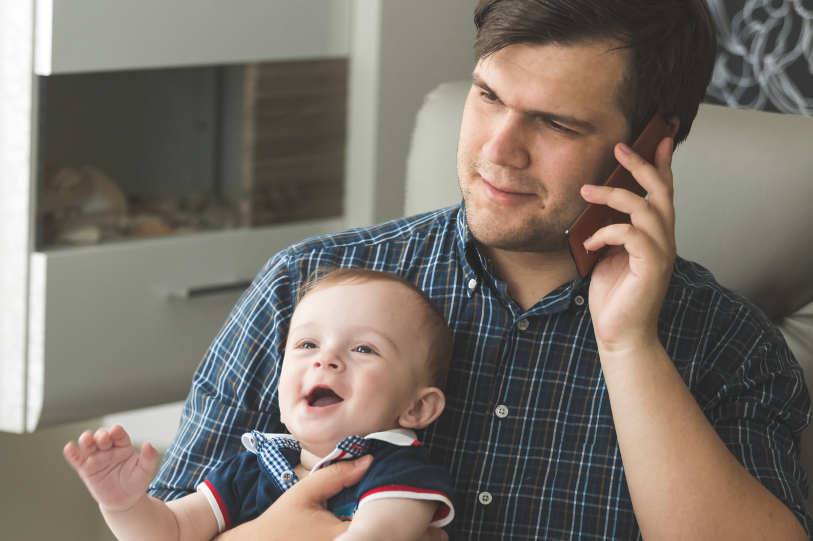 En man pratar i telefon. Han håller i ett litet barn.
