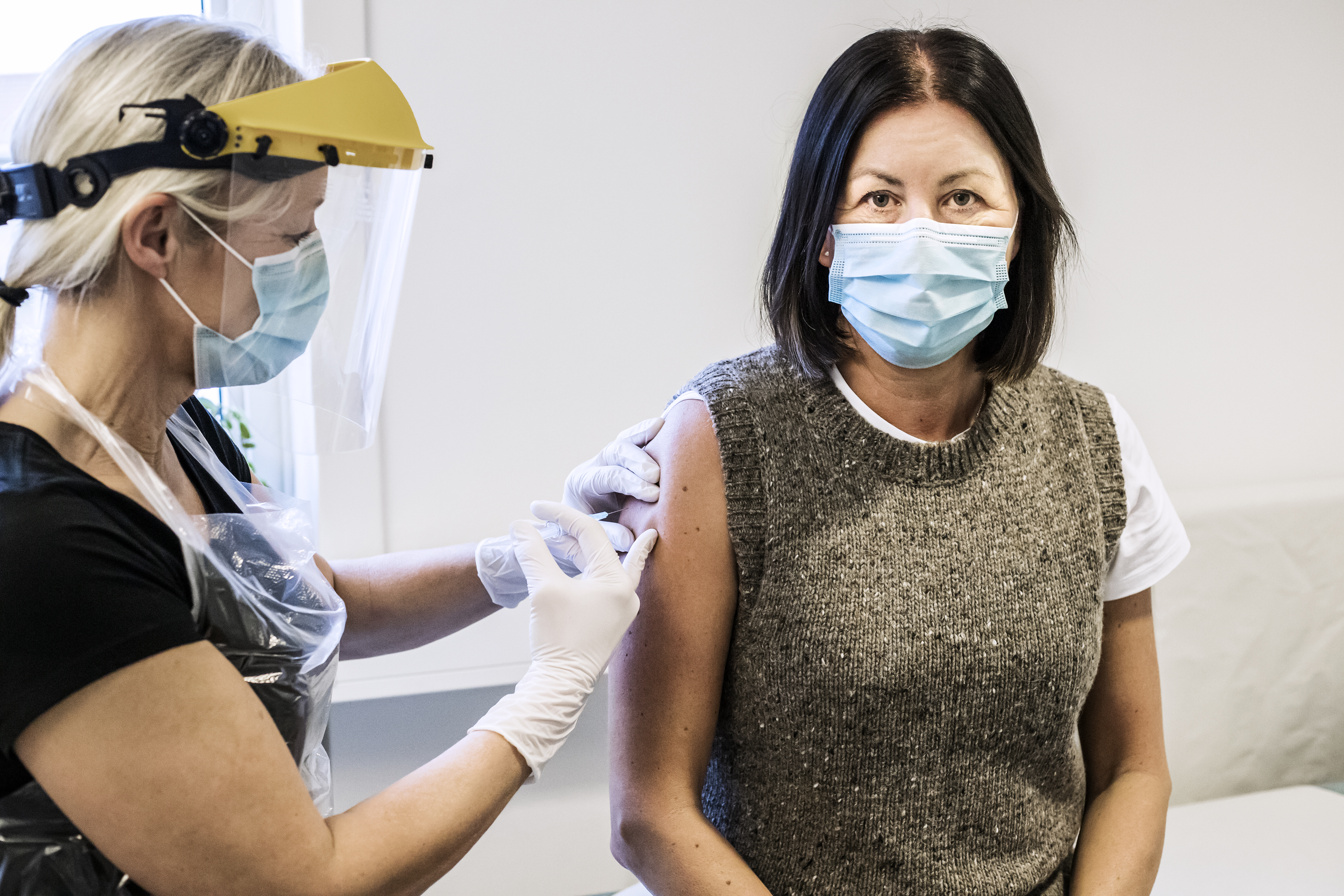 Kvinna som sitter och blir vaccinerad och bär munskydd