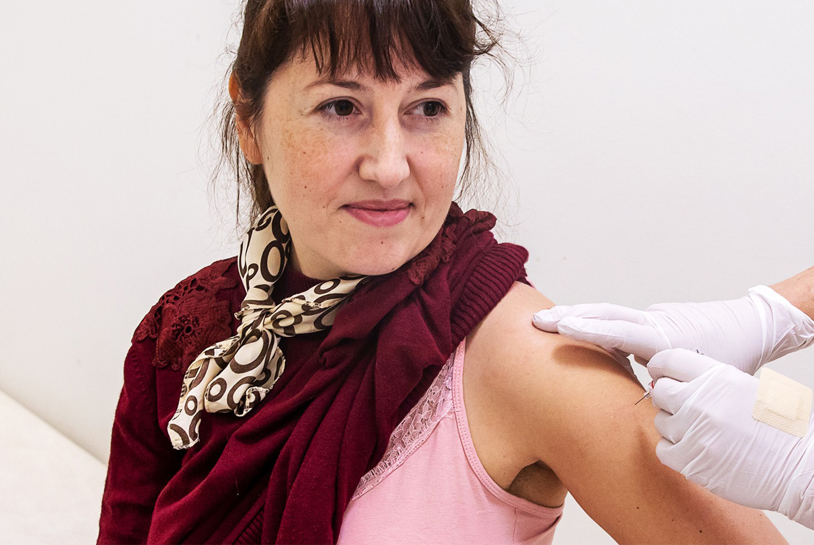 Kvinna som vaccinerar sig  med handskbeklädd hand i förgrunden