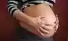 Kvinnan håller sina händer över en stor mage. Hon är långt gången i sin graviditet.