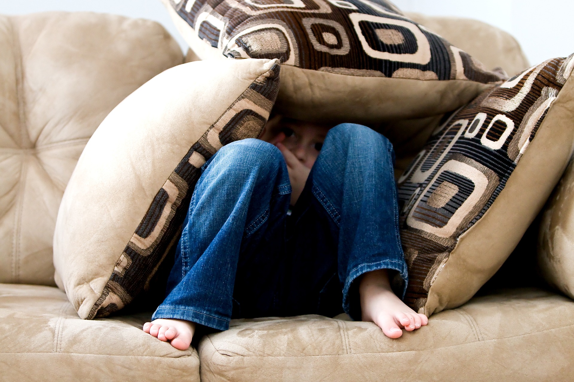 Rädd pojke gömmer sig bakom kuddar i en soffa