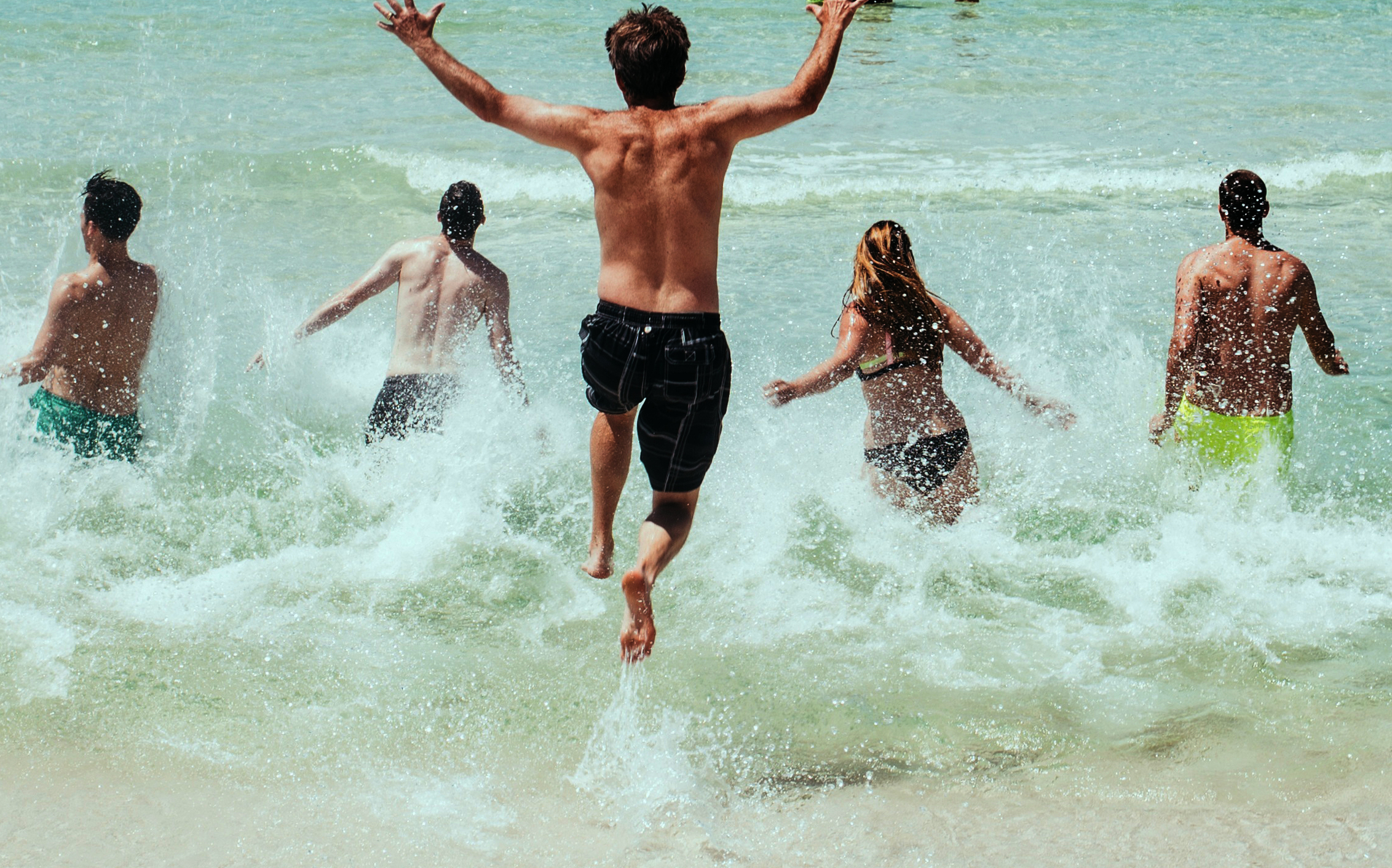 Ett gäng ungdomar rusar ner i vattnet vid en sandstrand