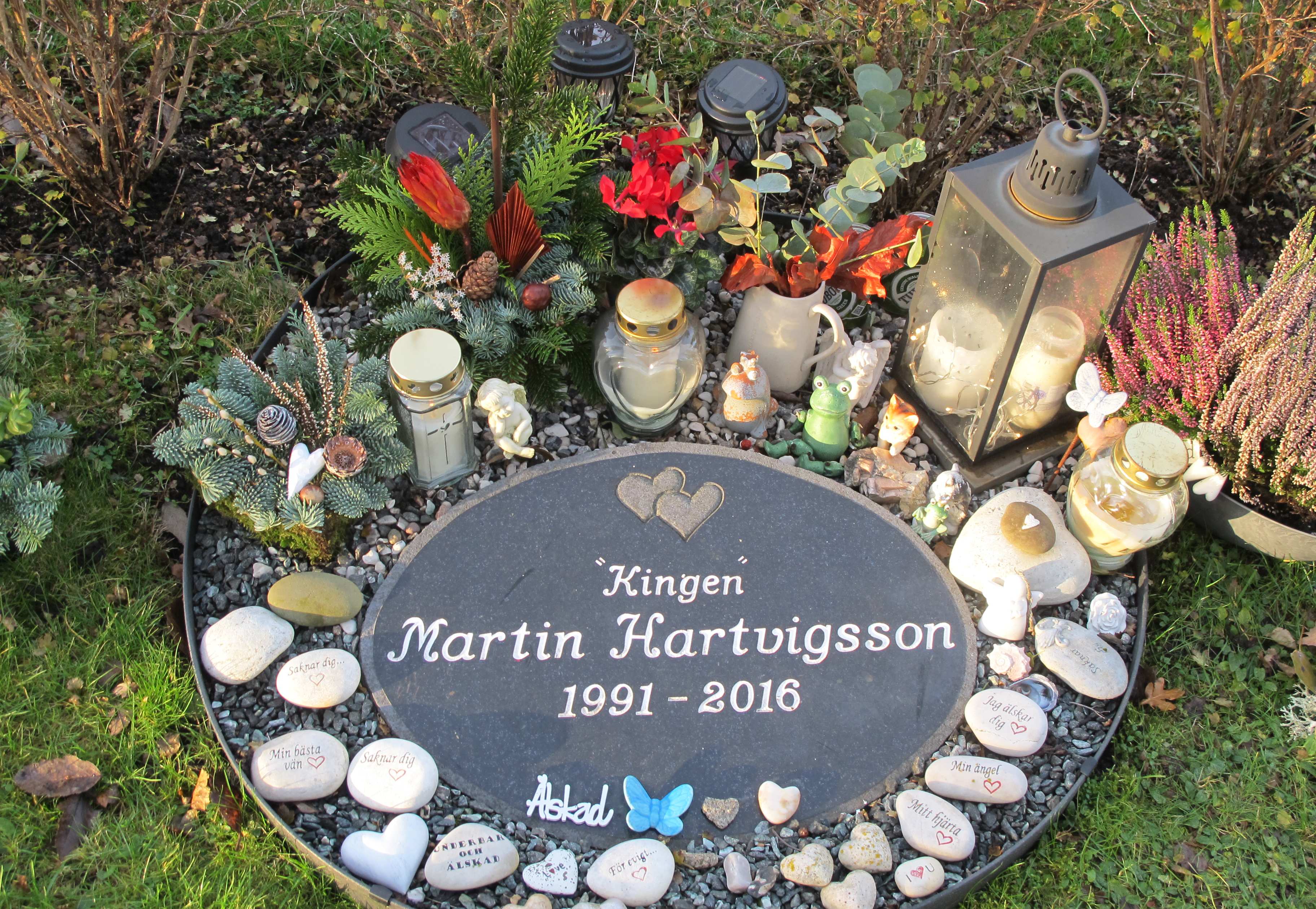 Nedsänt gravsten med namnet Martin Hartvigsson. Gravvård med mycket pynt.