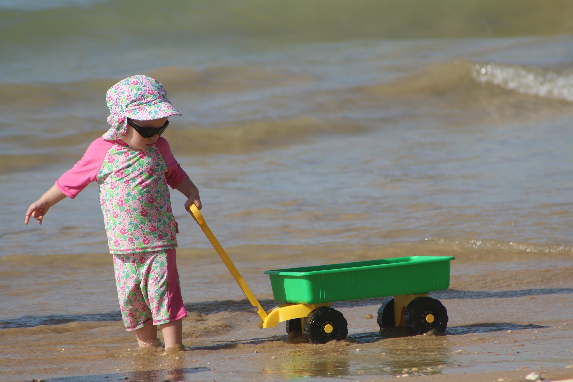Barn med kläder och solhatt drar en liten vagn längs med strandbrynet