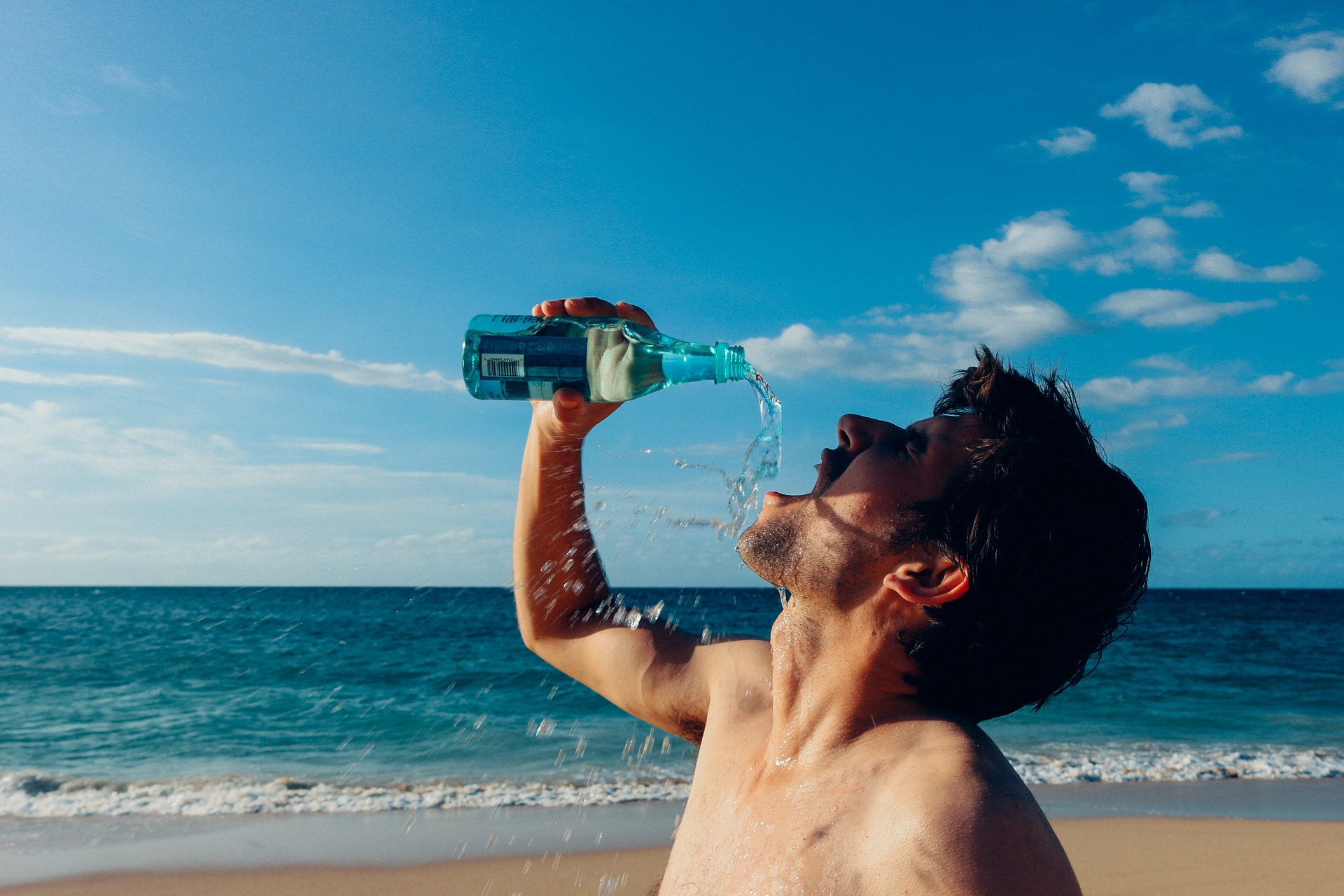 Kille på strand dricker ur flaska